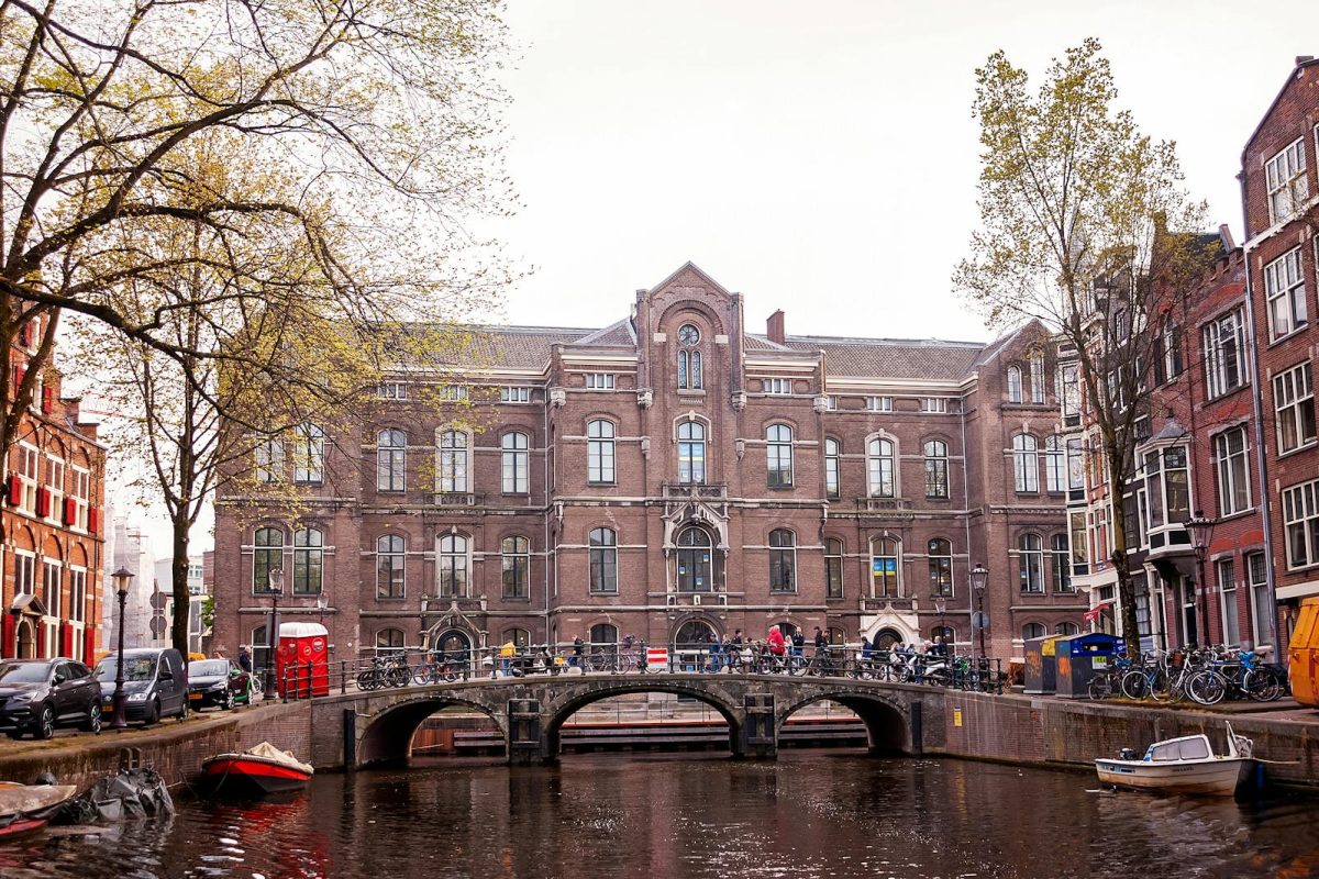 Historic Amsterdam canal with bridge and building facade, vibrant spring atmosphere.