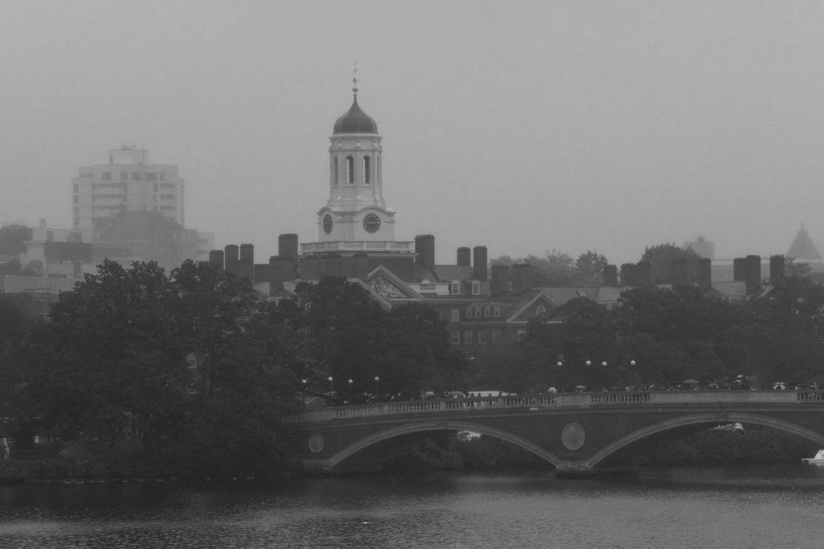 A foggy urban cityscape highlighting Harvard's iconic clock tower and Weeks Footbridge.
