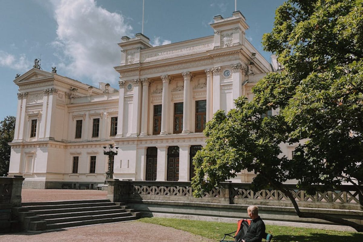 A man sitting on a bench outside the historic Lund University main building in Sweden.