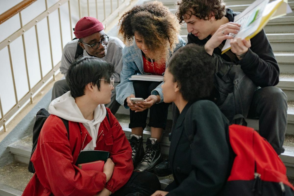 A group of diverse students sitting together on stairs, sharing a moment on a mobile device.